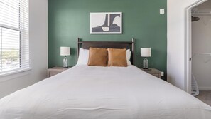 Ein Hotelzimmer mit einem großen Bett, zwei Nachttischlampen, einem Wandbild und Blick durch ein Fenster.