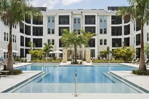 A hotel with a central swimming pool, surrounded by palm trees and lounge chairs. - Landing | Stunning 1BD, Yoga Studio, Gym (Punta Gorda)