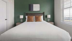 A hotel room with a large bed, two bedside lamps, a headboard, a painting on the wall, and a window with blinds. - Landing | Stunning 1BD, Yoga Studio, Gym (Punta Gorda)