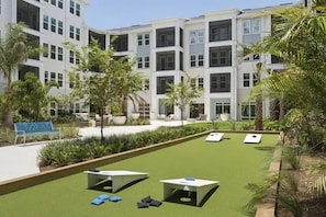 A courtyard with artificial grass, outdoor seating, and a modern building in the background. - Landing | Spectacular 1BD, Yoga Studio, Game Room (Punta Gorda)