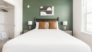 Habitación de hotel con una cama grande, dos lámparas de noche, una obra de arte en la pared y una ventana con persianas.