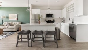 Una cocina moderna con armarios blancos, un refrigerador de acero inoxidable y un horno empotrado. Hay tres taburetes frente a la isla de la cocina.