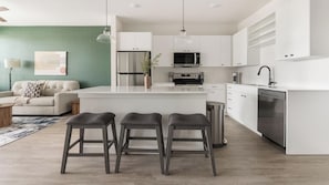 A modern kitchen with white cabinetry, a stainless steel refrigerator, and a built-in oven. There are three stools in front of the kitchen island. - Landing | Stylish 1BD, Game Room, Gym (Punta Gorda)