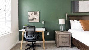 Quarto com cama, escrivaninha, cadeira, mesa de cabeceira e luminária na parede.