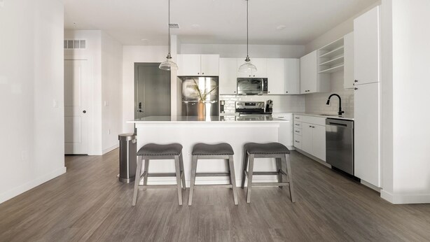 Cozinha moderna com armários brancos, eletrodomésticos de aço inoxidável e uma ilha central com banquetas.