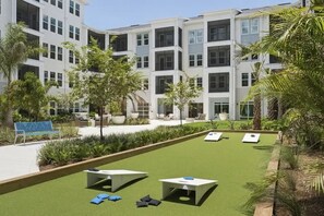 A courtyard with artificial grass, outdoor seating, and a modern building in the background. - Landing | Beautiful 1BD, Yoga Studio, Gym (Punta Gorda)