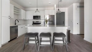 A modern kitchen with white cabinetry, stainless steel appliances, and a central island with bar stools. - Landing | Beautiful 1BD, Yoga Studio, Gym (Punta Gorda)