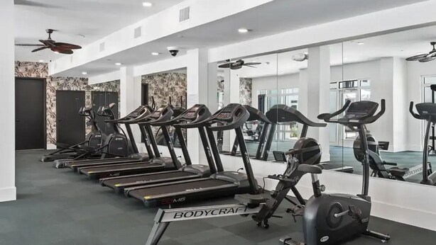 Une salle de sport équipée de plusieurs tapis de course et d’un appareil elliptique, avec des murs blancs et un ventilateur au plafond.