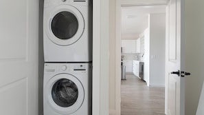 A laundry area with stacked washing machines and a view into a modern kitchen and living space. - Landing | Spectacular 2BD, Game Room, Yoga Studio (Punta Gorda)