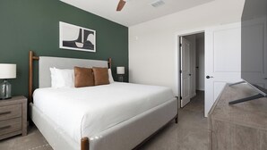 Une chambre à coucher bien rangée, avec un lit, des tables de chevet, une lampe et une porte donnant sur une autre pièce.