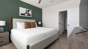 A neatly arranged bedroom with a bed, bedside tables, a lamp, and a door leading to another room. - Landing | Amazing 2BD, Yoga Studio, Game Room (Punta Gorda)