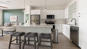 Une cuisine moderne avec des armoires blanches, des appareils en acier inoxydable et un îlot central doté de tabourets de bar.