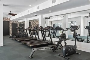 A gym with multiple treadmills and an elliptical machine, white walls, and a ceiling fan.