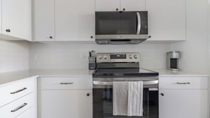 Een moderne keuken met witte kasten, een roestvrijstalen magnetron, een oven en een koffiezetapparaat.