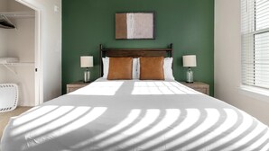 Un lit bien fait, avec une couette blanche, deux lampes de chevet et une tête de lit.