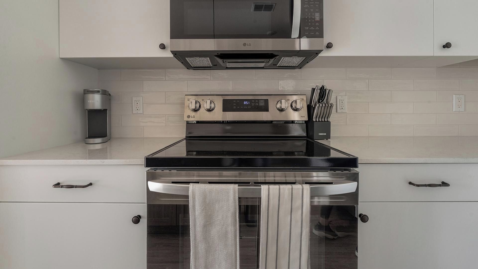 A modern kitchen with a stainless steel stove, oven, and microwave. There are two ovens, a coffee maker, and a knife block on the counter.