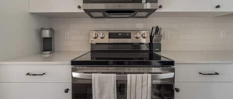A modern kitchen with a stainless steel stove, oven, and microwave. There are two ovens, a coffee maker, and a knife block on the counter.