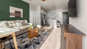 A modern living room with a sofa, coffee table, and a view into the kitchen. - Landing | Spectacular 2BD, Gym, Game Room (Punta Gorda)
