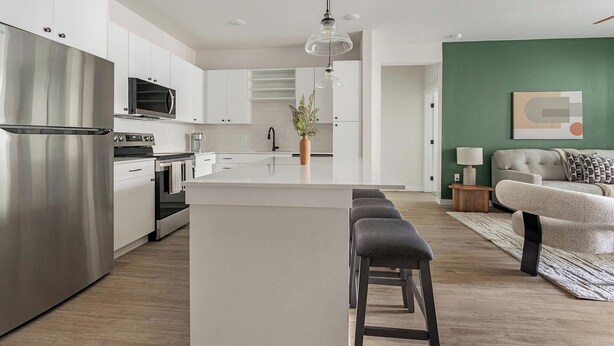 A modern kitchen with stainless steel appliances, a central island, and a dining area with a sofa and bar stools. - Landing | Stunning 2BD, Game Room, Gym (Punta Gorda)
