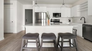 A modern kitchen with a central island, stainless steel appliances, and bar stools. - Landing | Beautiful 2BD, Game Room, Gym (Punta Gorda)