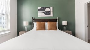 A hotel room with a large bed, two nightstands, a wall-mounted abstract art piece, and a window with blinds. - Landing | Chic 2BD, Yoga Studio, Game Room (Punta Gorda)