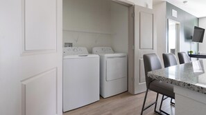 Une cuisine compacte dotée d’un lave-linge et d’un sèche-linge intégrés, d’un coin repas avec un plan de travail en marbre et d’un téléviseur à écran plat fixé au mur.