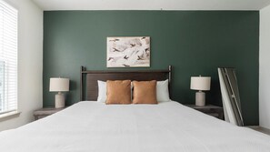 Une chambre à coucher avec un grand lit, deux tables de chevet, une lampe fixée au mur et une œuvre d’art encadrée au-dessus du lit.