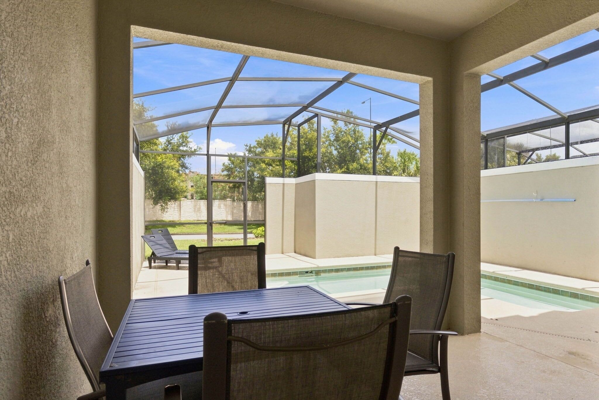 Un patio couvert avec une table et des chaises, une piscine et une vue sur le jardin arrière.