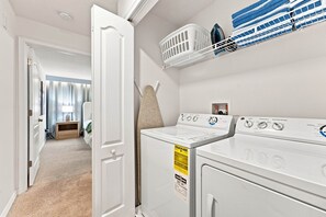A laundry room with a front-loading washer and dryer, a drying rack, and a wall-mounted ironing board. - Mickey & Mario Luxury Retreat, Private Pool (Kissimmee)