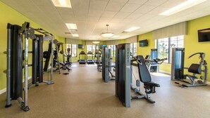 Ein Fitnessstudio mit verschiedenen Trainingsgeräten, großen Fenstern und einem gefliesten Boden.