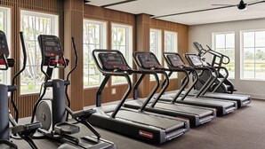 Ein Fitnessstudio mit Laufbändern und Crosstrainern, großen Fenstern und einem Deckenventilator.