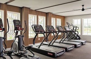 Ett träningscenter med löpband och crosstrainers, stora fönster och en takfläkt.