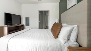 Ein Hotelzimmer mit Bett, Fernseher, Nachttisch und einer Tür zu einem Flur.