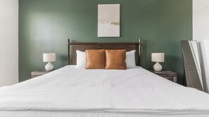 A neatly made bed with white bedding and two brown pillows, flanked by two bedside tables with lamps, against a green wall with a simple artwork above. - Landing | Incredible 2BD, Clubhouse, Pool (Port Charlotte)