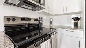 A modern kitchen with a black stove, stainless steel range hood, white cabinets, and a granite countertop. - Landing | Incredible 2BD, Clubhouse, Pool (Port Charlotte)
