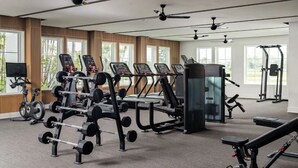 Ett modernt gym med olika typer av träningsutrustning, stora fönster och takfläktar.