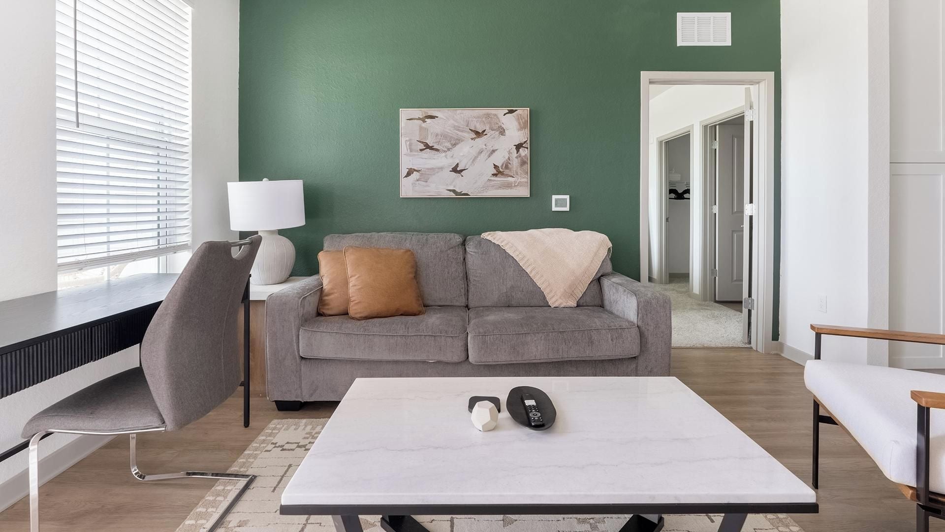 Un salon moderne avec un canapé gris, une table basse blanche et une lampe.