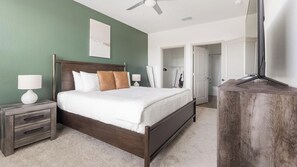 A bedroom with a bed, nightstands, a dresser, a ceiling fan, and a door leading to a bathroom. - Landing | Incredible 2BD, Clubhouse, Pool (Port Charlotte)