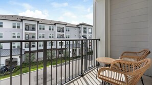 Een balkon met rieten stoelen, uitzicht op een meerhoog gebouw en een heldere lucht.