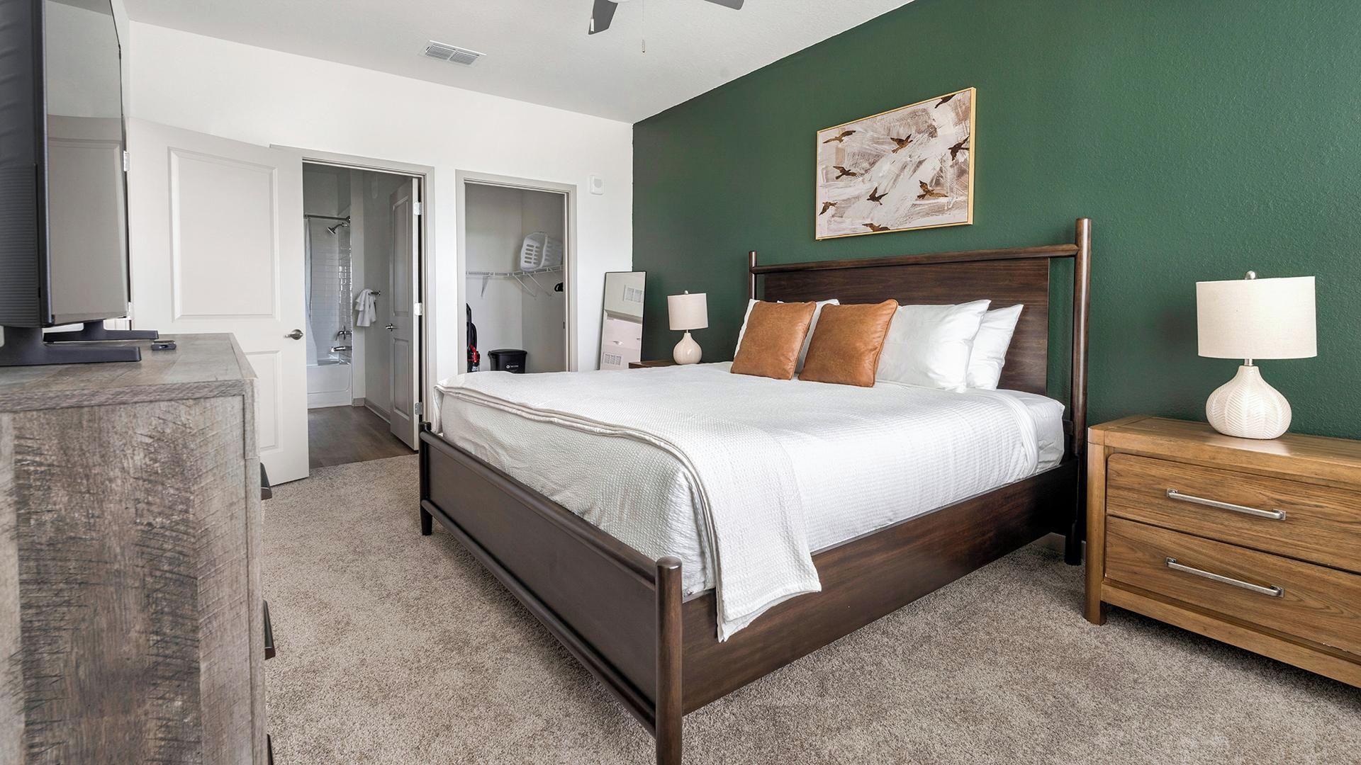 Een slaapkamer met een houten bed, een nachtkastje met lamp, een garderobe en een deur naar de badkamer.