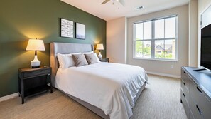 A bedroom with a bed, two bedside tables with lamps, a dresser, a TV, and a large window. - Landing | Amazing 2BD, Gym, Pool (Port Charlotte)