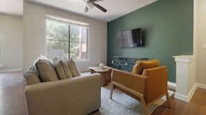 A living room with a sofa, a coffee table, and a TV mounted on the wall. - Landing | Amazing 2BD, Pool, Gym (Austin)