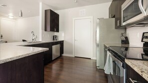 A modern kitchen with dark cabinetry, a stainless steel refrigerator, and a black stove. - Landing | Amazing 2BD, Pool, Gym (Austin)