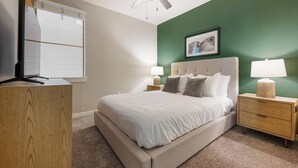 Een slaapkamer met een bed, nachtkastjes, een dressoir, een plafondventilator en een ingelijst schilderij aan de muur.