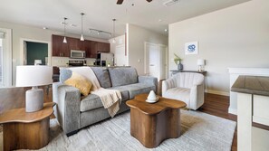 A modern living room with a grey sofa, wooden side tables, and a white armchair. - Landing | Stunning 2BD, Pool, Gym (Austin)