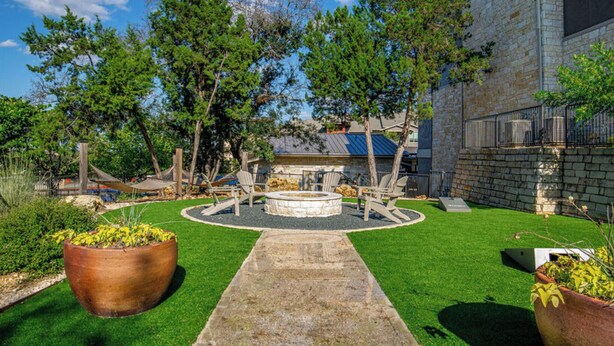 A landscaped backyard with a fire pit, seating area, and a stone wall. - Landing | Stunning 2BD, Pool, Gym (Austin)