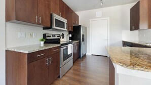 A modern kitchen with dark wood cabinets, stainless steel appliances, and granite countertops. - Landing | Stunning 2BD, Pool, Gym (Austin)
