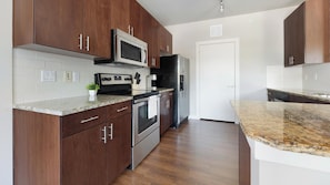 A modern kitchen with dark wood cabinets, stainless steel appliances, and granite countertops. - Landing | Stunning 2BD, Pool, Gym (Austin)