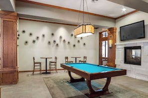 Uma mesa de bilhar com cadeiras, uma televisão e uma lareira numa sala com vigas de madeira e decoração de parede.