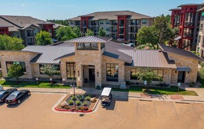 A multi-story building with a stone facade, large windows, and a parking lot with cars. - Landing | Stylish 2BD, Gym, Pool (Austin)